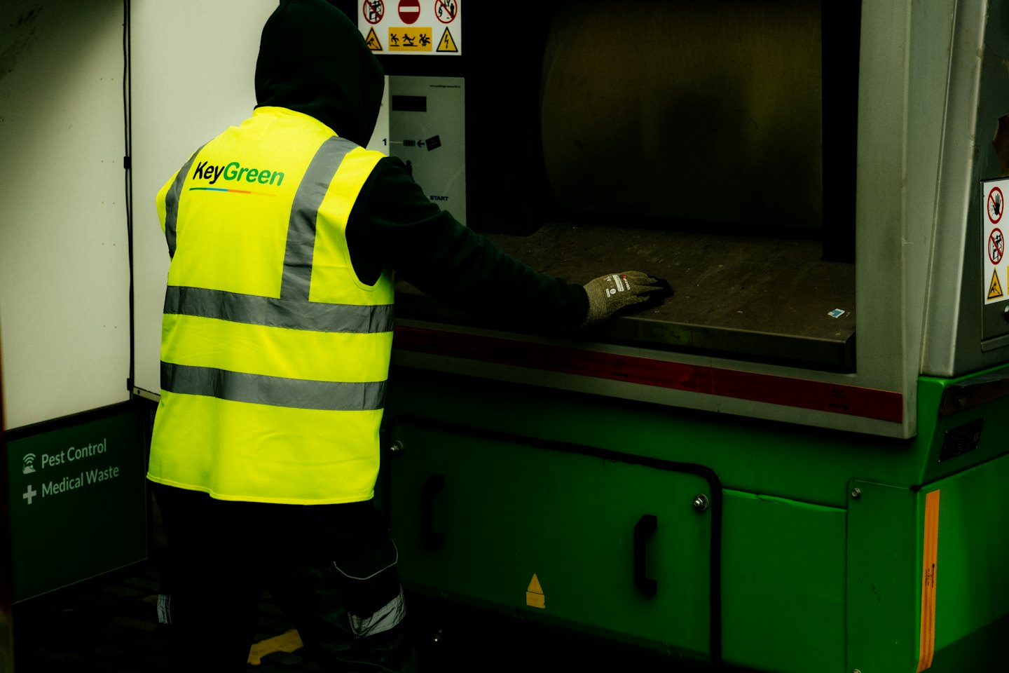 Operaio con giubbotto di sicurezza che utilizza un macchinario per rifiuti industriali.
