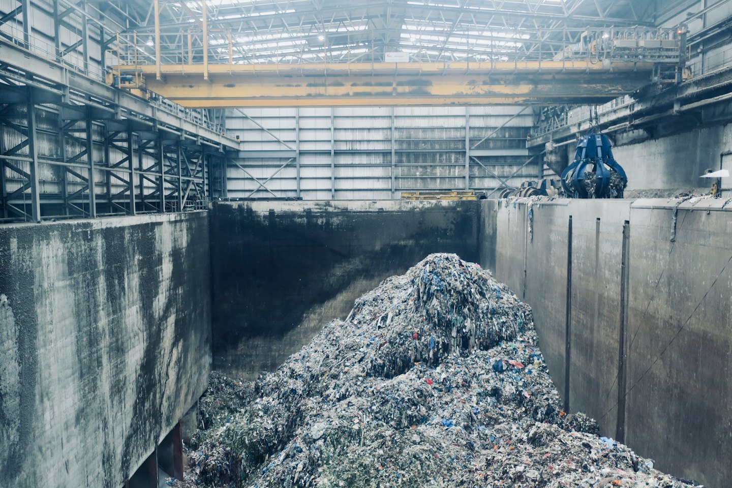 Pinza di una gru su rifiuti industriali in una vasca di cemento.